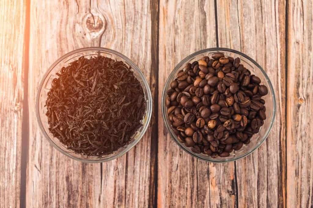 Two bowls of coffee beans on a wooden table, showcasing why coffee is better than tea.